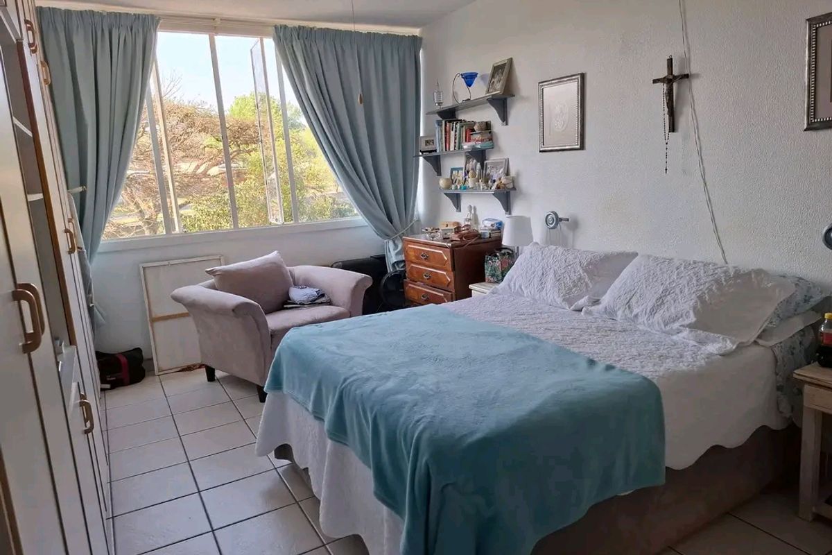 A functional bedroom featuring tiled flooring, a large window providing natural light, and built-in wardrobe storage.