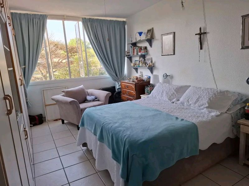 A functional bedroom featuring tiled flooring, a large window providing natural light, and built-in wardrobe storage.