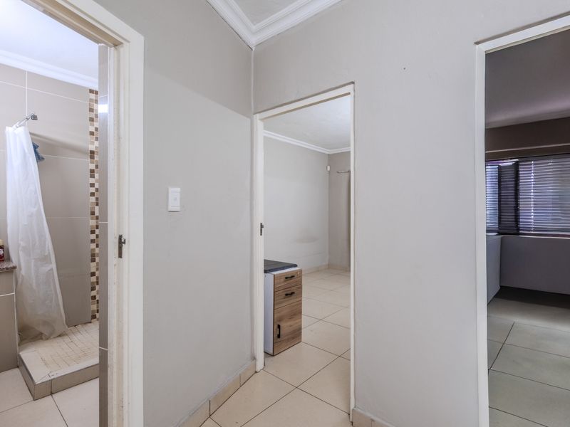 A neutral hallway providing access to a bathroom and adjacent rooms, featuring tiled flooring and clean wall finishes.