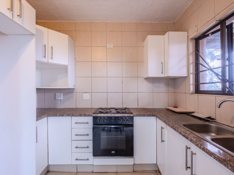 A functional kitchen featuring white cabinetry, laminate countertops, a built-in electric oven and hob, and a double bowl sink with tiled splashback.