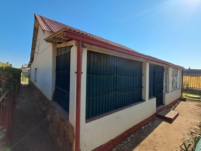 Rear exterior view of the house featuring a corrugated metal roof, stone cladding base, and security bars on the windows.