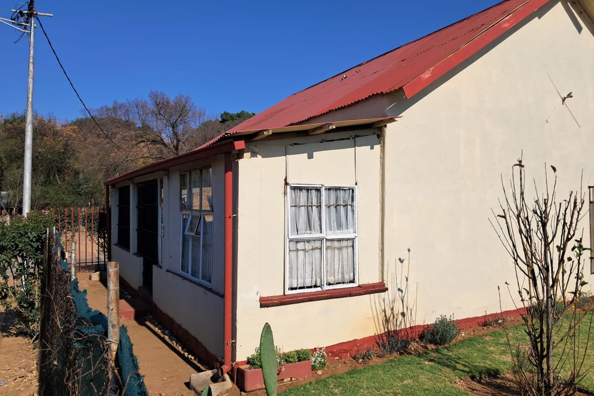 Side view of a residential house featuring a red corrugated metal roof, plastered walls, and traditional casement windows with security bars.