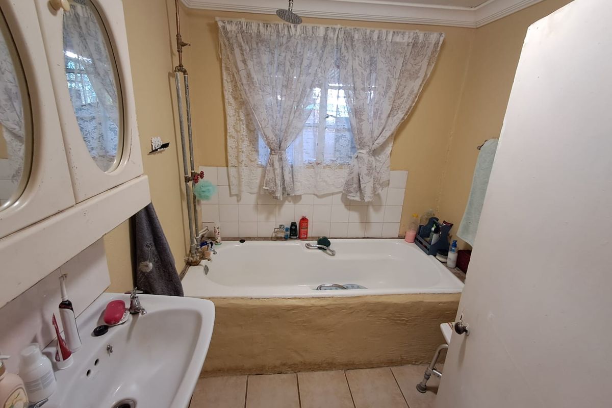 A dated bathroom featuring a built-in bathtub with exposed shower plumbing, a pedestal sink, and tiled flooring, offering potential for a modern renovation.