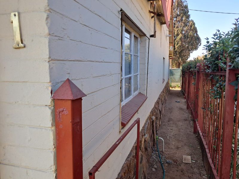 Side exterior view of the property featuring stone cladding, painted brick walls, and a metal perimeter fence along a narrow pathway.