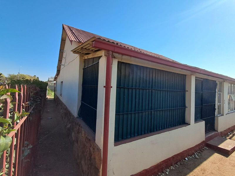 Rear exterior view of the house featuring a corrugated metal roof, stone cladding base, and security bars on the windows.