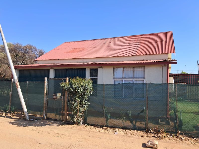 Front exterior view of a single-story house featuring a corrugated metal roof and chain link perimeter fencing.