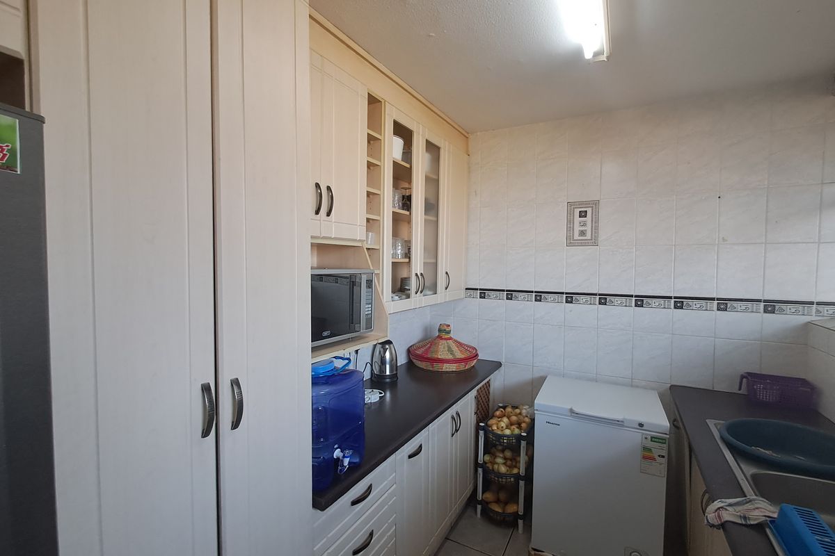 A functional kitchen featuring light-toned built-in cabinetry, laminate countertops, tiled backsplash, and a double sink, offering practical storage and workspace.