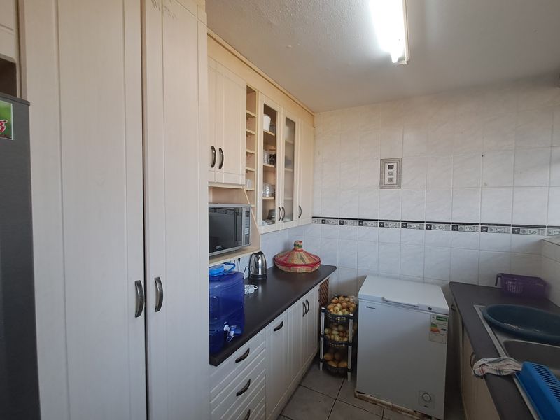 A functional kitchen featuring light-toned built-in cabinetry, laminate countertops, tiled backsplash, and a double sink, offering practical storage and workspace.