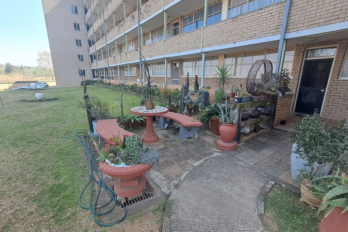 A rear exterior view of an apartment building featuring a paved patio area, brick facade, and a concrete walkway leading to the entrance.