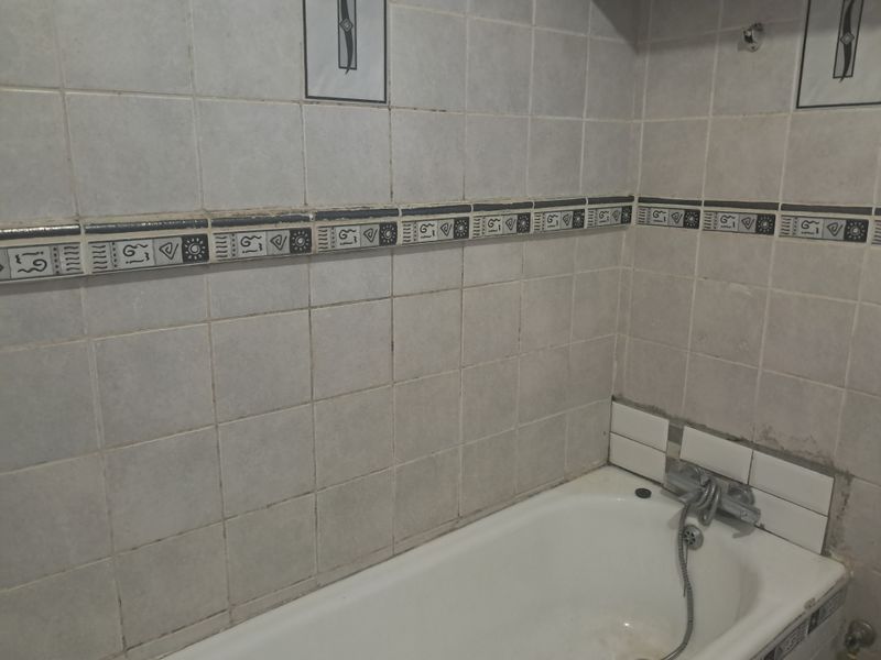 A dated bathroom featuring a standard bathtub with a shower mixer and decorative ceramic wall tiling.