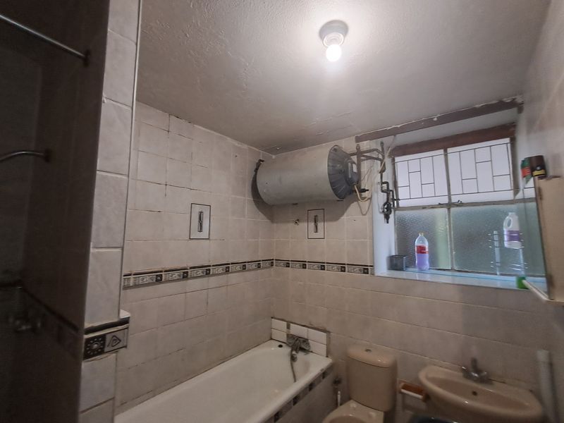 A dated bathroom featuring a bathtub, pedestal basin, toilet, and wall-mounted electric water heater with visible plumbing.