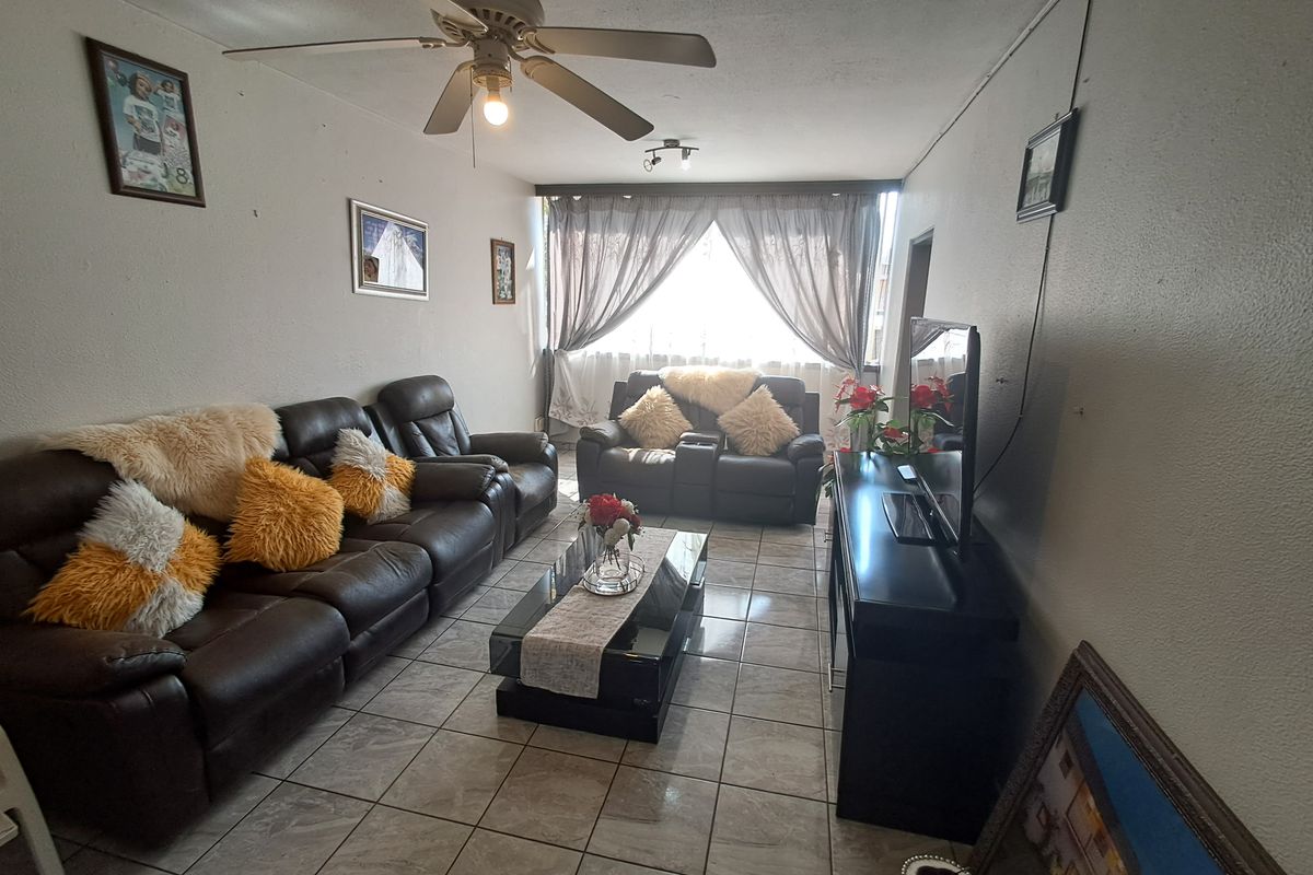 A living room featuring ceramic tile flooring and a ceiling fan, offering a functional space with potential for cosmetic updates.
