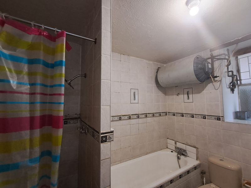 A functional bathroom featuring a built-in bathtub, shower area, and wall-mounted electric water heater, requiring cosmetic updates to modernize the space.