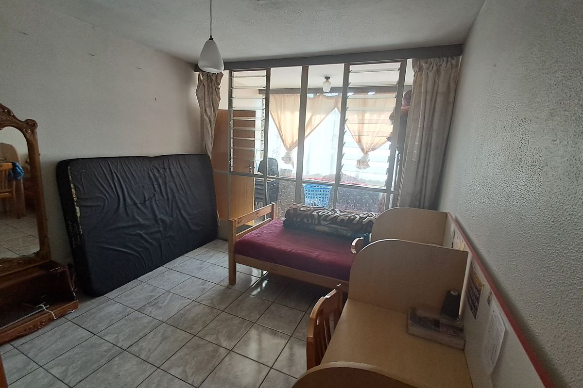 A bedroom featuring tiled flooring and a large window with security bars, requiring cosmetic updates to the walls and ceiling to improve its overall condition.