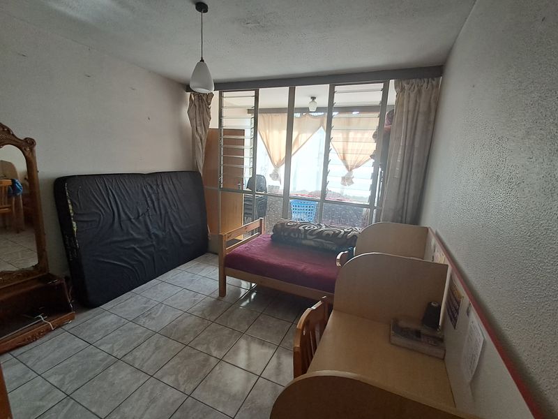 A bedroom featuring tiled flooring and a large window with security bars, requiring cosmetic updates to the walls and ceiling to improve its overall condition.