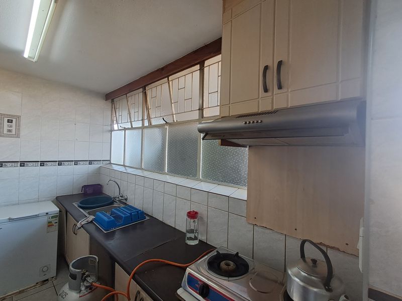 A functional kitchen featuring built-in cabinetry, a stainless steel extractor fan, tiled splashbacks, and a single basin sink with natural light.