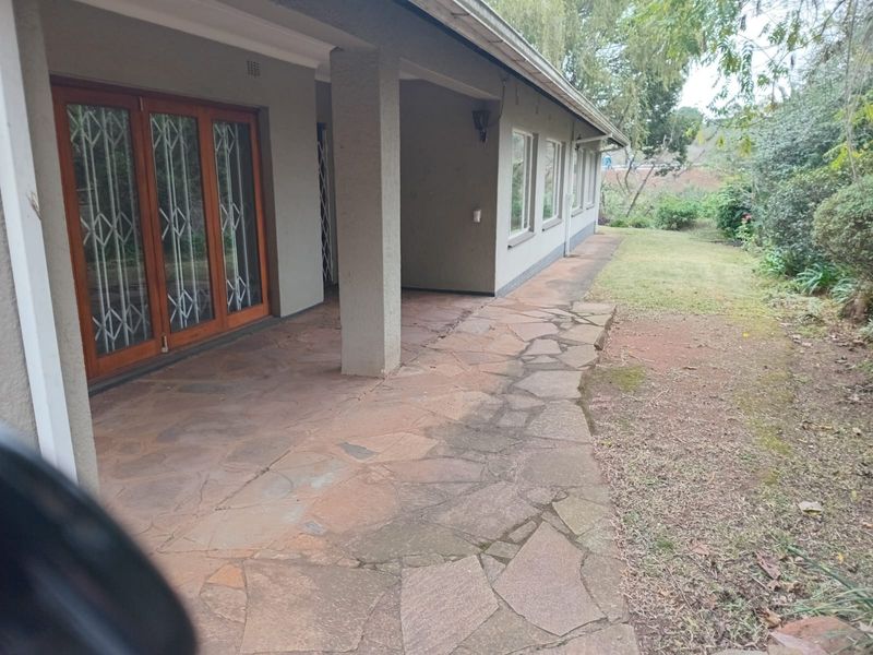 A covered patio area featuring flagstone paving and wooden sliding doors, providing direct access to the rear garden.