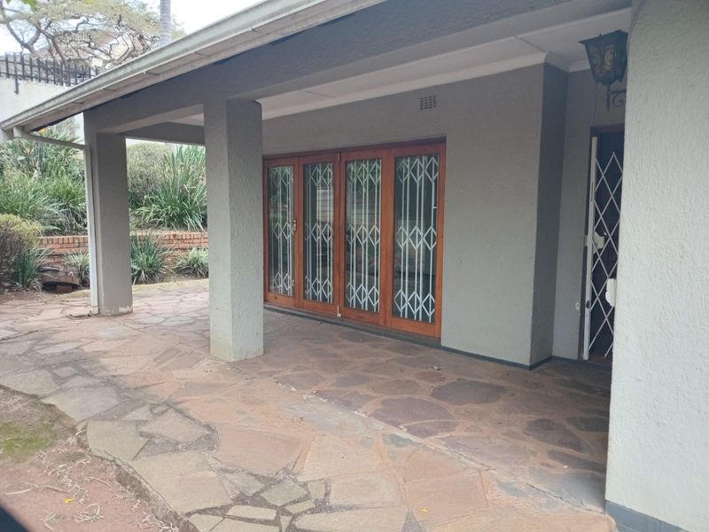 A covered patio area featuring stone paving, concrete support pillars, and wooden folding doors with security gates.