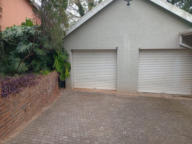 A double garage with roller doors, featuring a brick-paved driveway and a landscaped retaining wall.