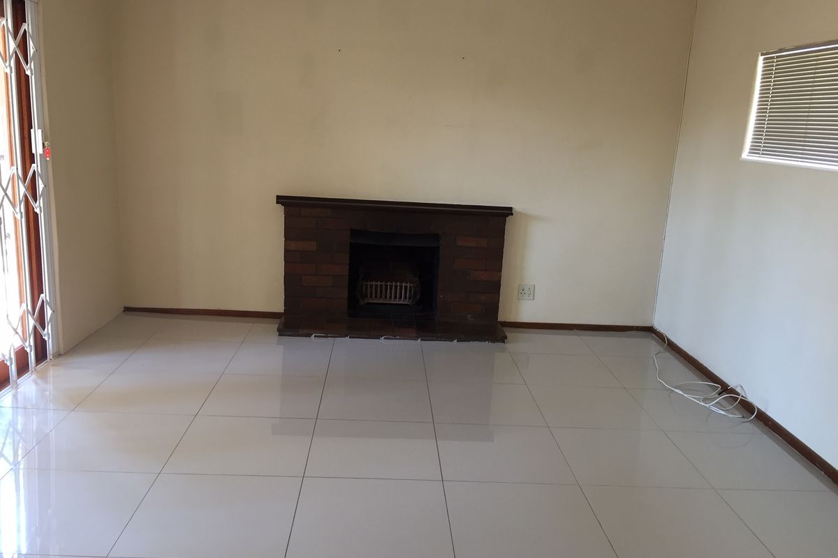 An empty living room featuring tiled flooring, a brick fireplace, and a sliding glass door with a security gate.