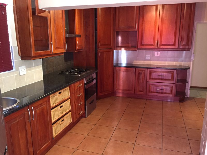 A functional kitchen featuring warm-toned wooden cabinetry, granite countertops, a gas hob, built-in oven, and tiled flooring throughout.