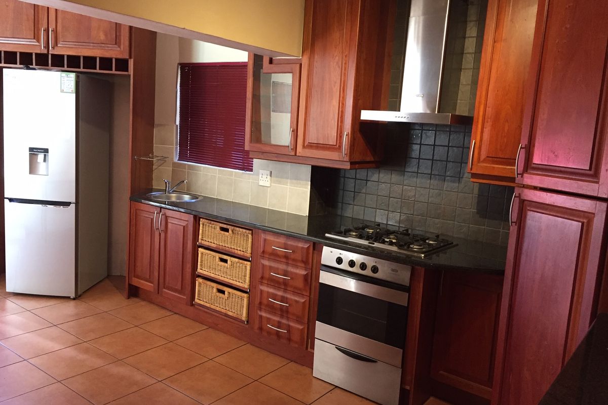 A functional kitchen featuring warm-toned wooden cabinetry, granite countertops, a gas hob, and a stainless steel extractor fan with tiled flooring.