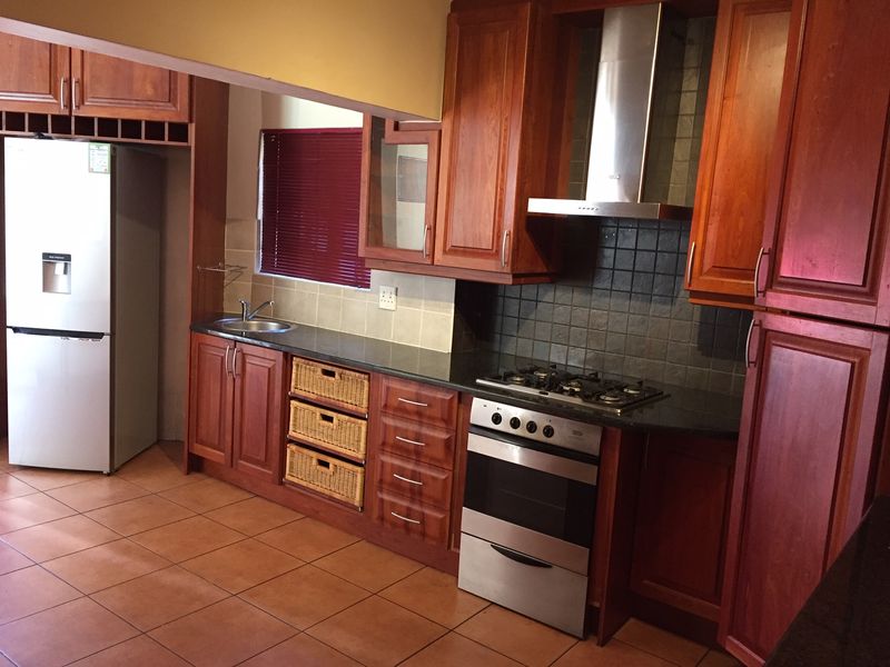 A functional kitchen featuring warm-toned wooden cabinetry, granite countertops, a gas hob, and a stainless steel extractor fan with tiled flooring.