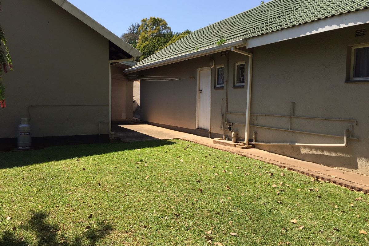 Rear exterior view of the property featuring a lawn, concrete pathway, and tiled roof structure with visible external plumbing.