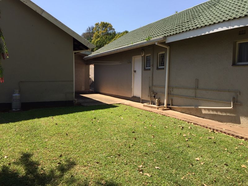 Rear exterior view of the property featuring a lawn, concrete pathway, and tiled roof structure with visible external plumbing.