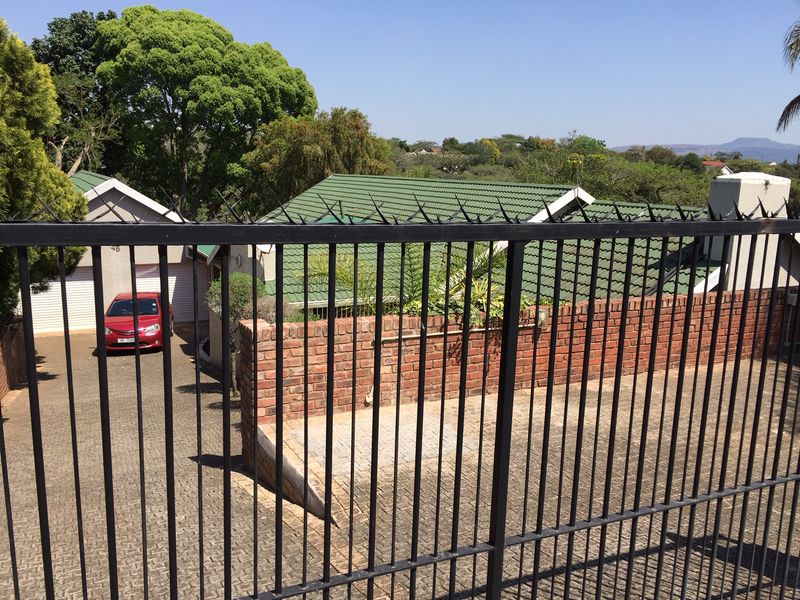 Front view of the property featuring a paved driveway, garage, and secure perimeter fencing with a brick boundary wall.