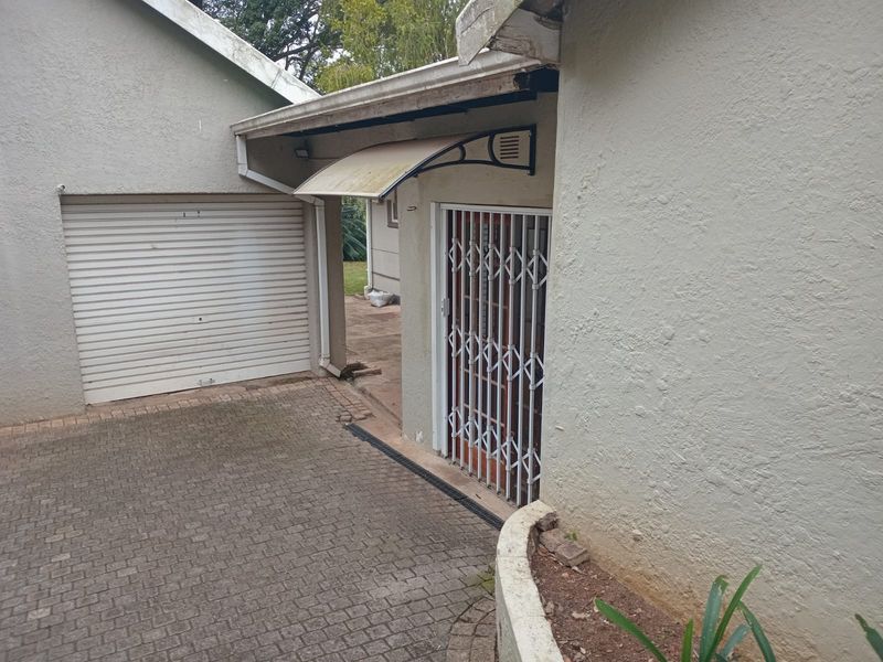 Exterior view of the property featuring a paved driveway, a roller garage door, and a side entrance protected by a security gate and awning.