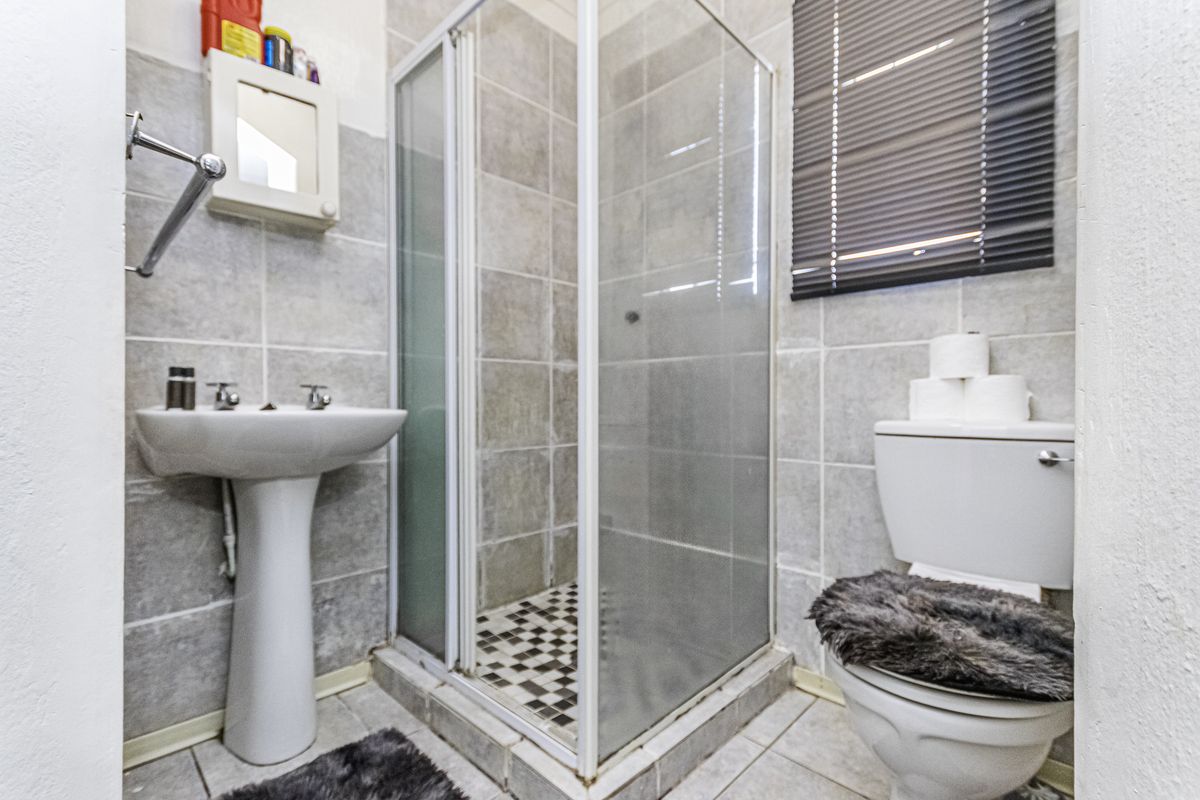A functional bathroom featuring a pedestal washbasin, a glass-enclosed shower, and a toilet, finished with neutral wall and floor tiling.
