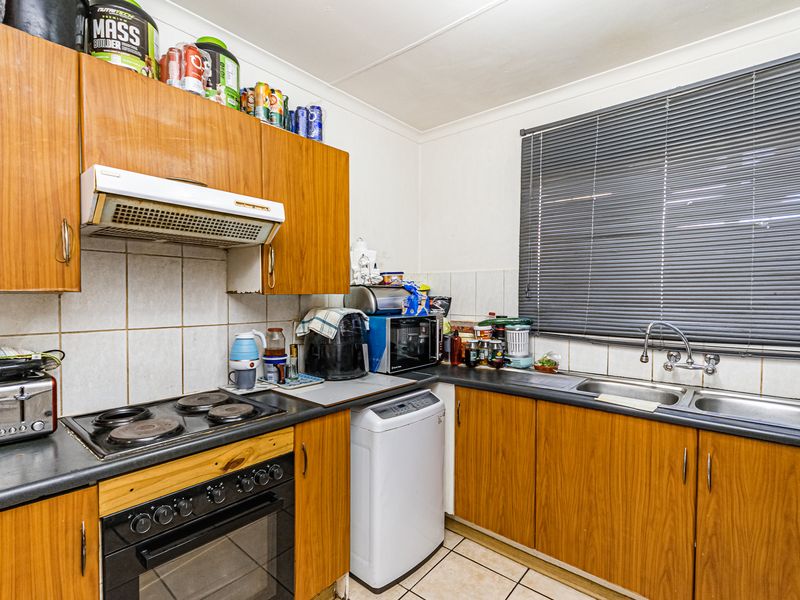 A functional kitchen featuring wood-look laminate cabinetry, a built-in oven with electric hob, double stainless steel sink, and tiled splashbacks.