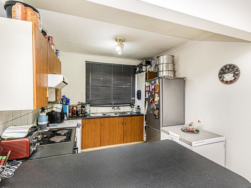 Compact kitchen featuring wooden cabinetry, laminate countertops, a stainless steel sink, and an integrated electric hob with an extractor fan.
