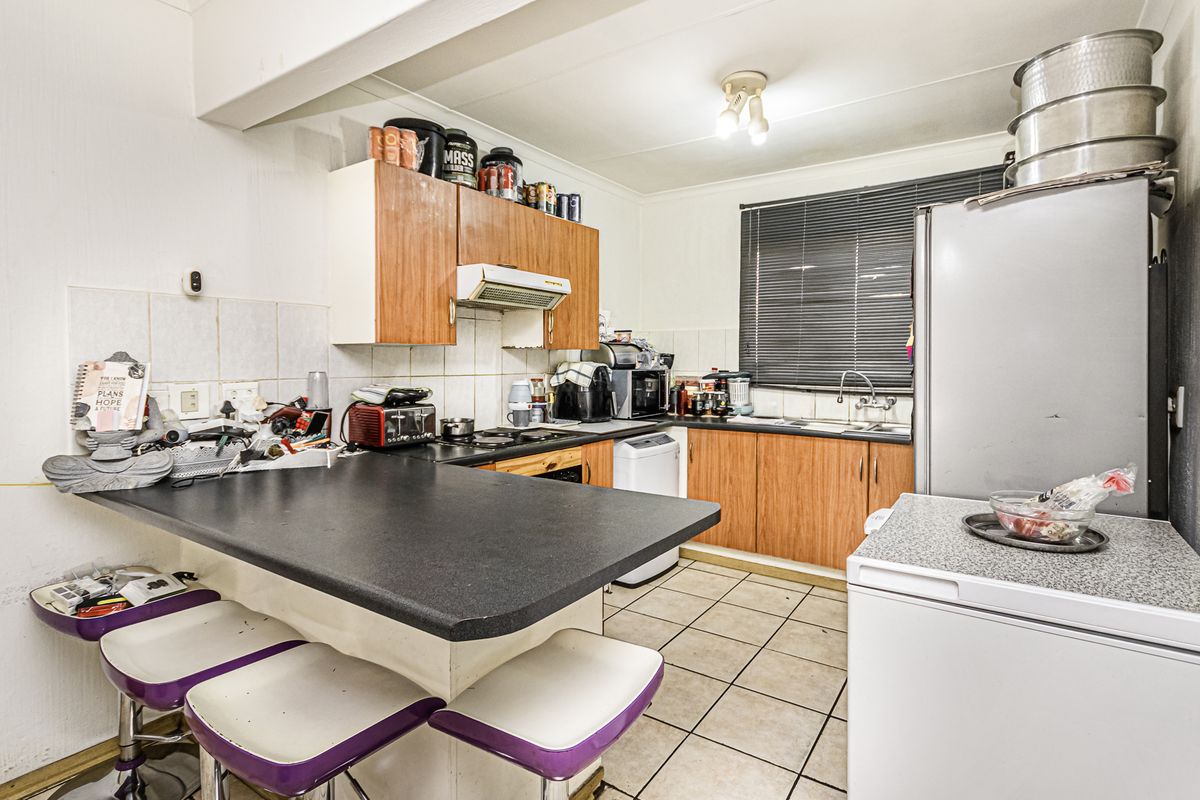 A functional kitchen featuring laminate cabinetry, a breakfast bar, tiled backsplash, and ceramic flooring, offering potential for modernization and aesthetic updates.