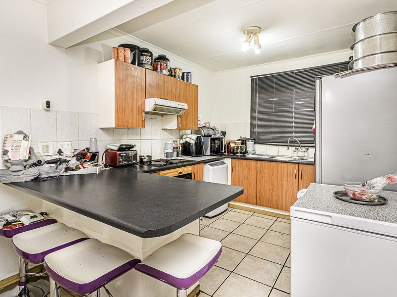 A functional kitchen featuring laminate cabinetry, a breakfast bar, tiled backsplash, and ceramic flooring, offering potential for modernization and aesthetic updates.