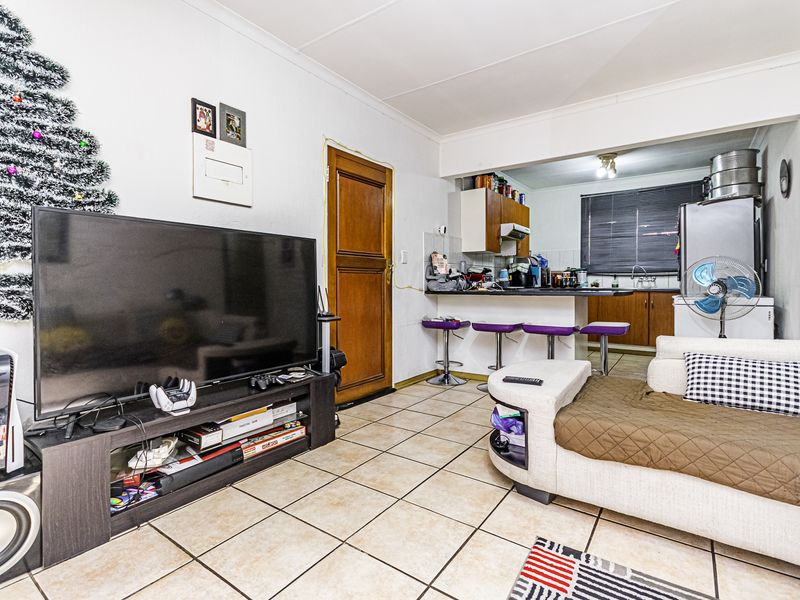 Open-plan living area featuring tiled flooring, a breakfast counter, and a functional kitchen with built-in cabinetry and an extractor fan.
