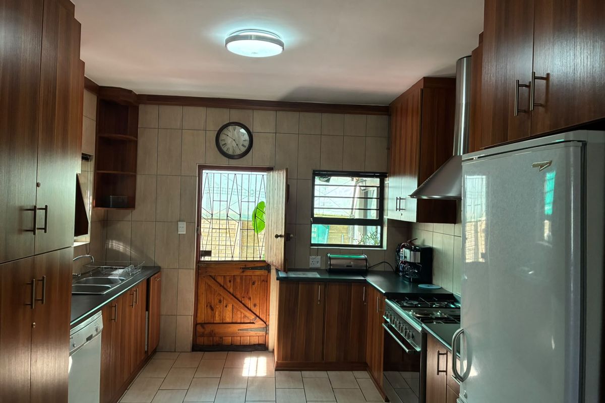 A functional kitchen featuring warm-toned wooden cabinetry, dark laminate countertops, a gas stove with extractor fan, and tiled flooring with direct outdoor access.