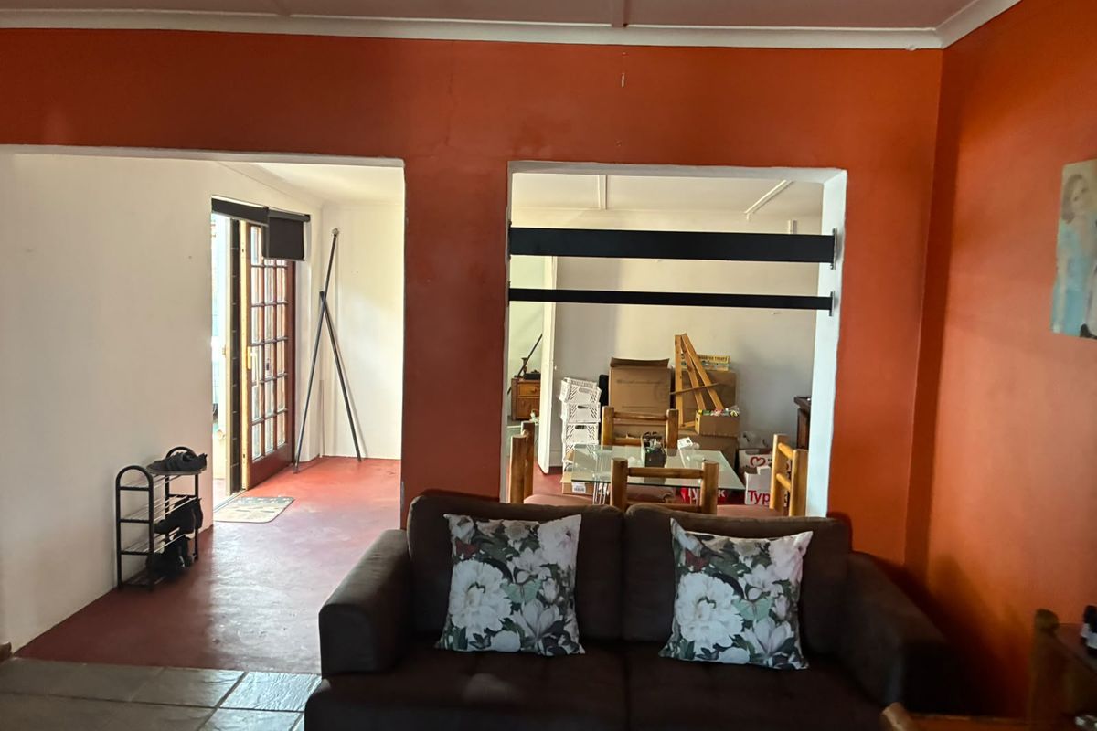 Living room area featuring tiled flooring and access to an adjacent space through a large wall opening, with a timber-framed glass door leading outside.
