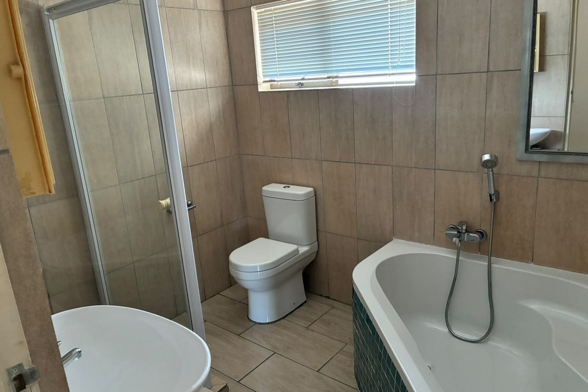 A functional bathroom featuring a shower enclosure, bathtub, toilet, and basin with neutral wall and floor tiling.