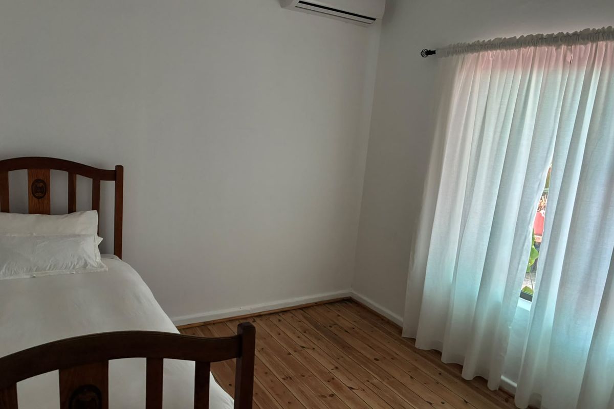 A bright bedroom featuring polished timber flooring and a wall-mounted split-system air conditioning unit.