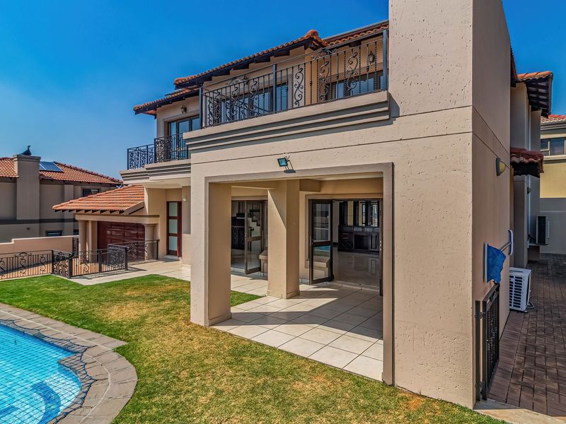 Rear view of the property featuring a covered patio, upper balcony with wrought iron railings, swimming pool, and landscaped garden area.