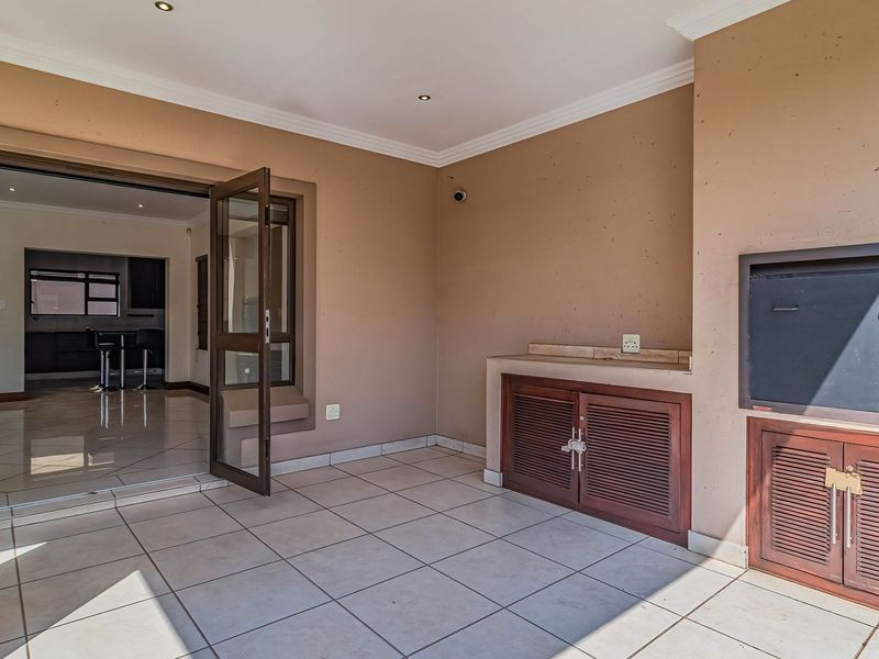 Covered patio featuring tiled flooring, built-in braai, and cabinetry, with direct access to the interior living space through sliding glass doors.