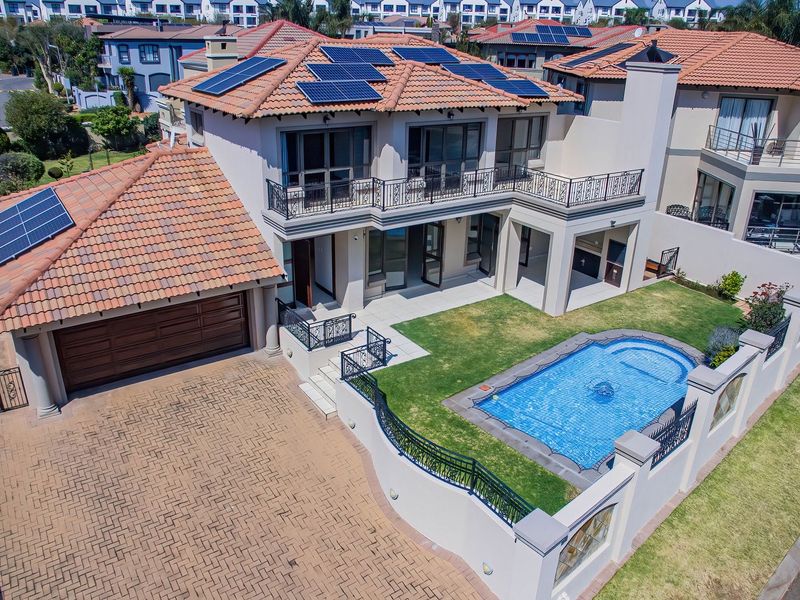 Aerial view of a modern residential property featuring a tiled roof with solar panels, a swimming pool, paved driveway, and a balcony.