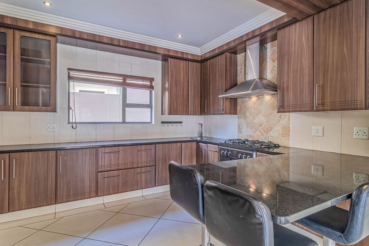 Modern kitchen featuring wood-finish cabinetry, granite countertops, a gas hob with extractor fan, and a convenient breakfast nook for casual dining.