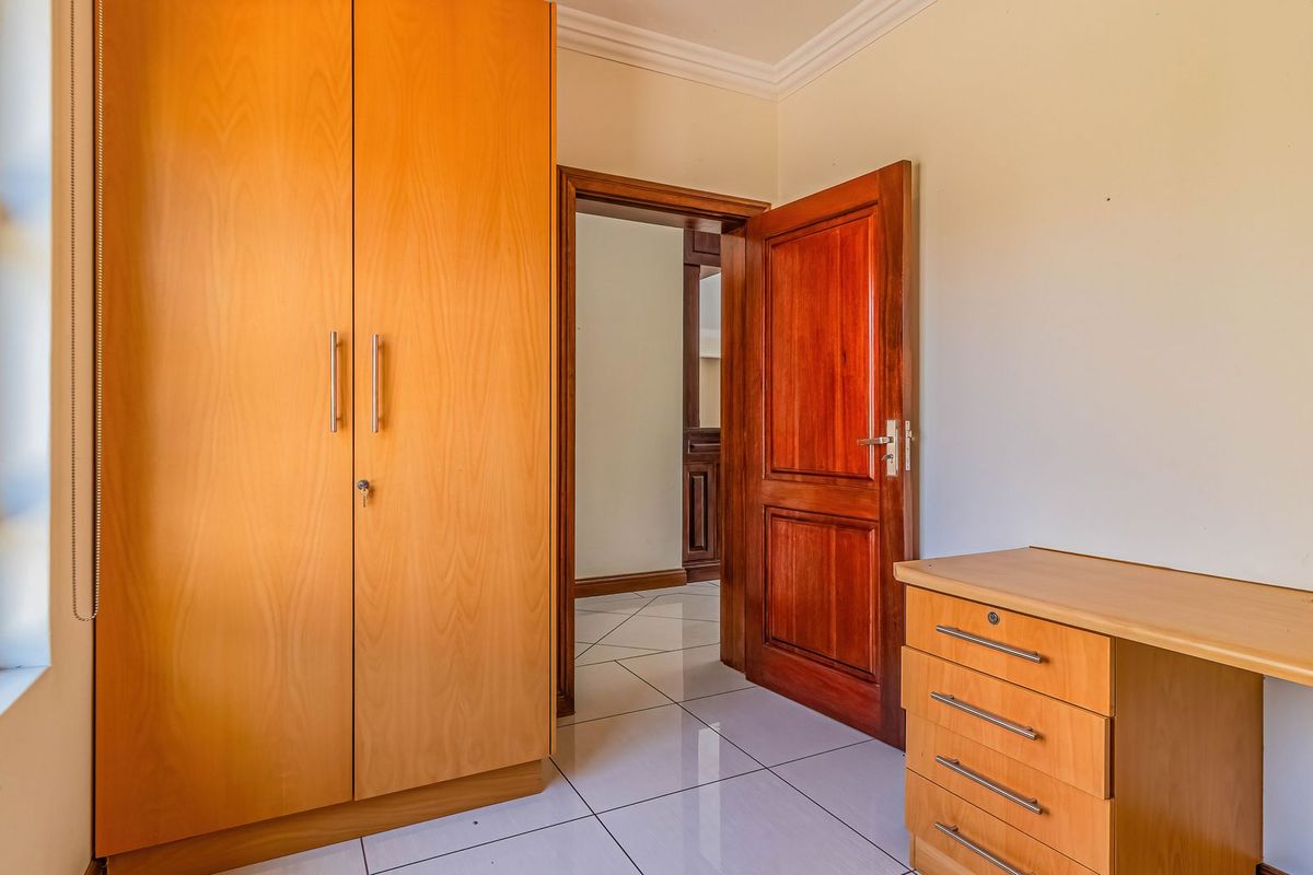 A bedroom featuring tiled flooring, a built-in wooden wardrobe, and a solid timber door, providing a clean and functional living space.