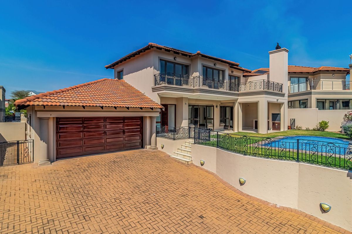 Rear view of a multi-story house featuring a swimming pool, paved driveway, double garage, and upper-level balconies with wrought iron railings.