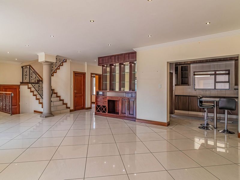 Spacious open-plan living area featuring tiled floors, a built-in bar, and a staircase with a decorative wrought iron balustrade leading to the upper level.
