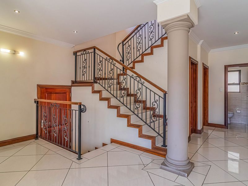 Spacious entrance hall featuring a grand staircase with wrought iron balustrades, polished tiled flooring, and a decorative column.
