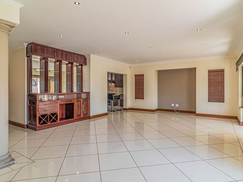 Spacious open-plan living area featuring polished tiled floors, a built-in wooden bar unit, recessed lighting, and neutral finishes throughout.